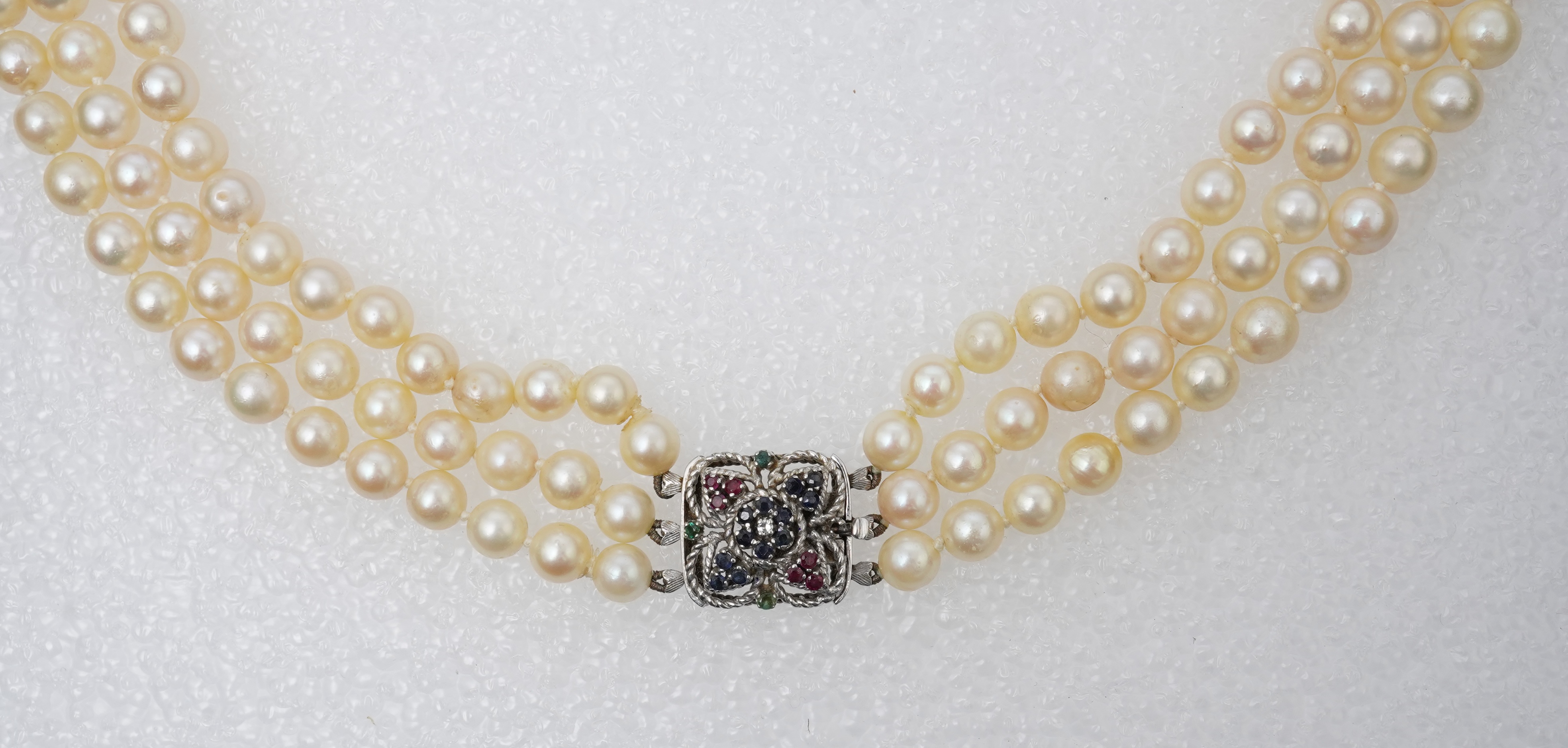 A mid to late 20th century Italian triple strand cultured pearl necklace, with emerald, sapphire and ruby cluster set 750 white metal clasp, 44cm.